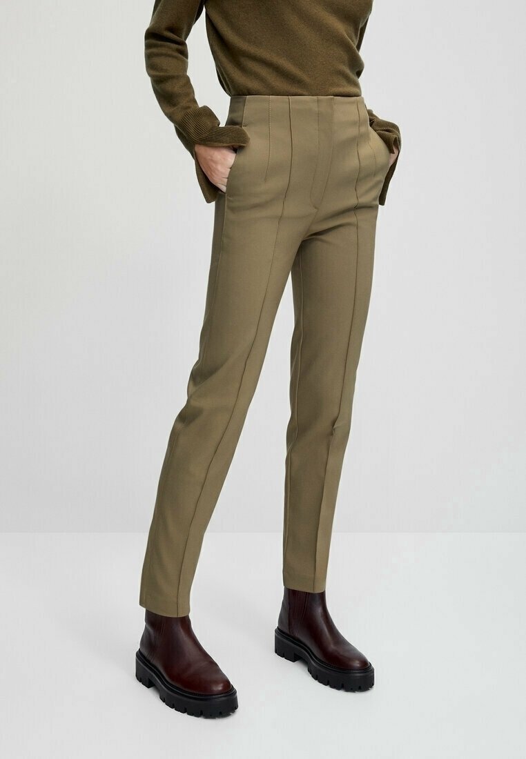 Pantalon beige sur mesure avec coutures verticales, coupe slim, taille haute, associé à des bottines marron à semelle épaisse.