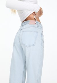 Jeans de mezclilla azul claro con un corte relajado, que cuentan con un parche de cuero rosa en la parte trasera y bolsillos traseros estándar. La tela parece suave.