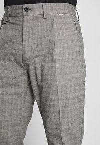 Pantalones estructurados grises de patrón de cuadros, con frente plano, dos bolsillos laterales y cierre de un botón con cremallera.