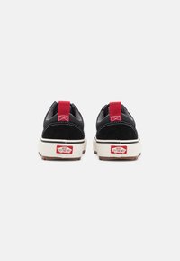 Svarte semskede og mesh sneakers med en rød draetab, hvit mellomsåle og brun gummisåle. Med merkevarelogo på hælen.