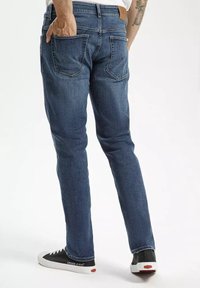 Granatowe dżinsy w slim fit, z skórzaną metką z tyłu oraz klasycznym pięciopocketowym wzorem. W zestawie z czarnymi sneakersami.