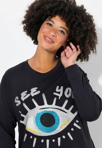 Zwarte sweatshirt met een groot oogontwerp in combinatie met blauwe, zwarte en gele accenten, versierd met zilveren pailletten en geribde manchetten.