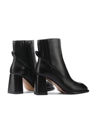 Stivali ankle in pelle nera con punta rotonda, tacco a blocco spesso e dettagli a coste sul retro. Chiusura con zip su un lato.