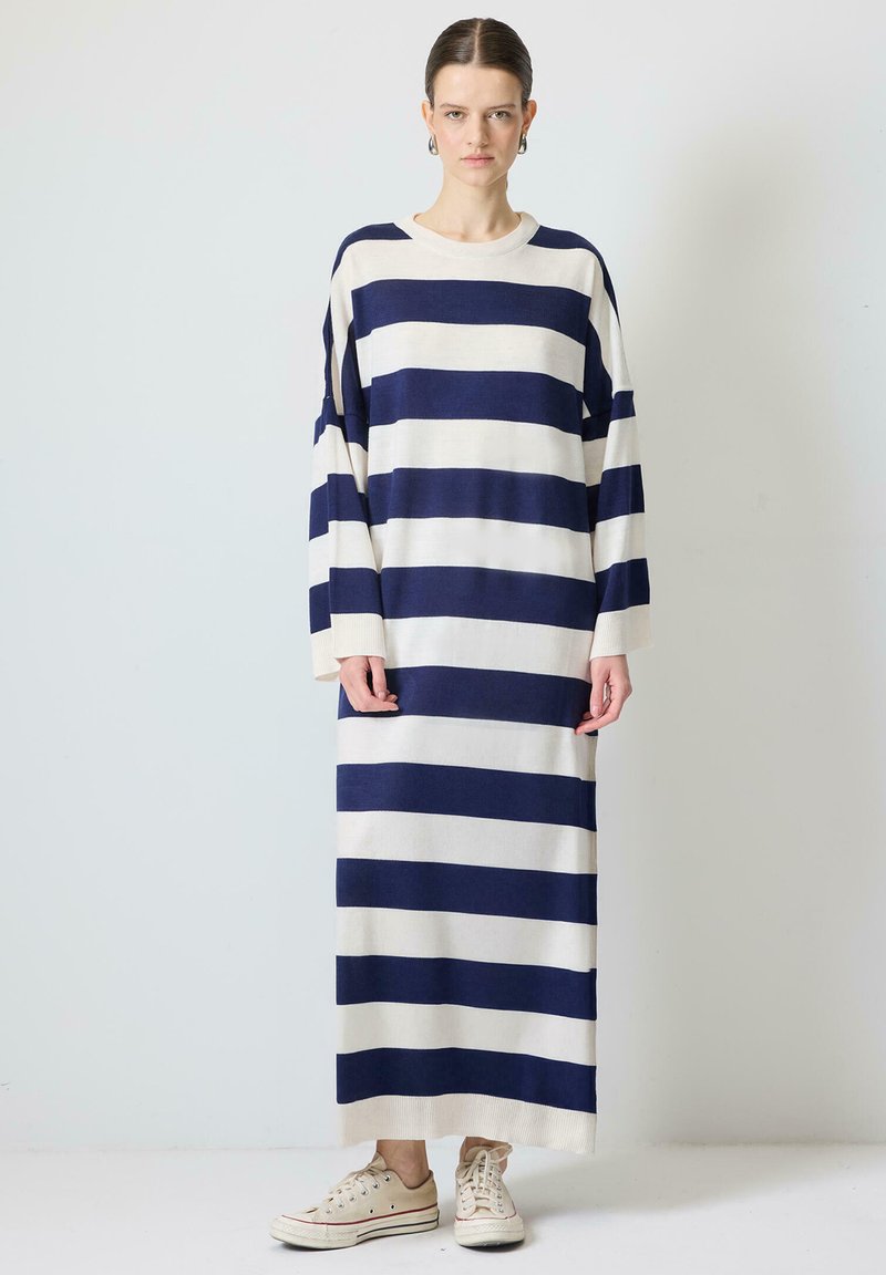 Rochie lungă în dungi, de culoare bleumarin și crem, realizată dintr-un material moale. Prezintă mâneci largi, o croială lejeră și un decolteu rotund. Stilizată cu teniși bej.
