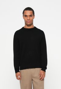 Sweater de gola redonda preto em um tecido macio, com mangas longas e um corte relaxado. A barra é ligeiramente mais longa na parte de trás.