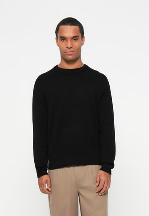 Black crewneck sweater in a soft fabric, featuring long sleeves and a relaxed fit. The hem is slightly longer at the back.