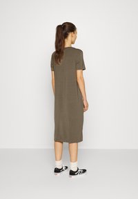 Vestido verde-azeitona, de mangas curtas e corte casual, que chega até à meia panturrilha. Combinado com sapatilhas pretas e meias brancas. Design simples, em cor sólida.