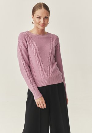 Light pink knitted sweater featuring a cable knit design with textured patterns, ribbed cuffs, and hem. Paired with black wide-leg trousers.