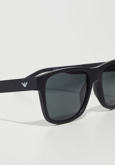 Ochelari de soare dreptunghiulari negri cu lentile colorate, fabricați din plastic. Au un design minimalist și un logo pe braț.