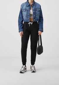 Džínová krátká bunda, šedý crop top, černé tepláky s bílým stahovacím páskem a vzorované tenisky. Doplňky: malá černá kabelka.