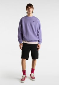 Sudadera morada con cuello redondo, pantalones cortos negros, calcetines rojos de Vans y zapatillas con estampado. Estilo casual urbano.