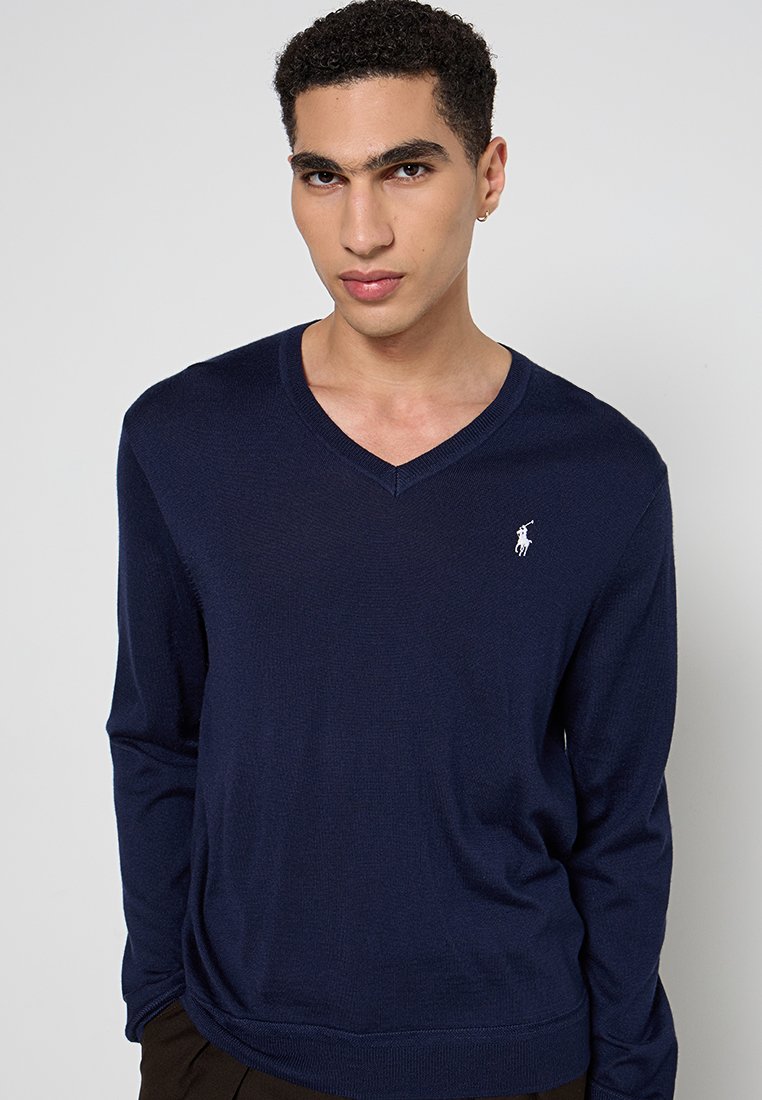 Maglione a maglia blu navy con scollatura a V, maniche lunghe e un piccolo logo bianco sul lato sinistro del petto. Texture liscia, materiale leggero.