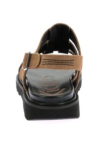Sandales en cuir marron avec une sangle texturée, boucle réglable et semelle en caoutchouc noire ; présentent des coutures complexes sur la sangle.