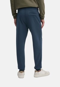 Pantalones de chándal azul marino con un corte ajustado, cinturilla elástica y un bolsillo trasero. Hechos de tela suave, combinados con zapatillas de color claro.