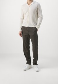 Cardigan leggero di colore crema, lavorato a maglia, con colletto a scollo e bottoni, abbinato a pantaloni scuri e sneakers bianche.