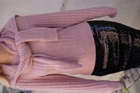 Helles rosa, geripptes Strickoberteil mit umgeschlagenem Kragen; dazu ein schwarer Paillettenrock mit vertikalen bunten Mustern.