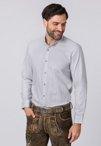 Hellgraues Hemd mit Karomuster, das einen Hemdkragen und braune Knöpfe aufweist, getragen mit dunklen braunen Lederhosen mit kunstvollen Details.