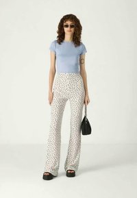 Ανοιχτού μπλέ κοντομάνικο μπλουζάκι συνδυασμένο με ψηλόμεσα λευκά παντελόνια που διαθέτουν μαύρο ανάγλυφο σχέδιο. Το μοντέλο κρατά μια μικρή μαύρη τσάντα.