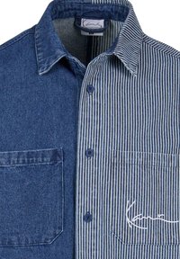 Chemise boutonnée avec un côté en denim bleu uni et l’autre côté rayé vertical bleu et blanc, avec poches poitrine avant et col.