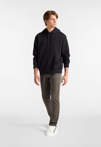 Sudadera negra con bolsillo frontal y cordones, combinada con pantalones verde oliva y zapatillas blancas con un detalle de raya.