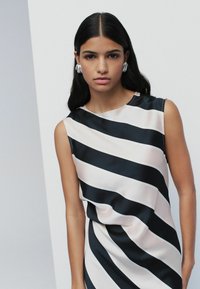 Vestido satinado a rayas negras y crema con escote redondo y diseño sin mangas, que presenta tela drapeada y una textura suave.