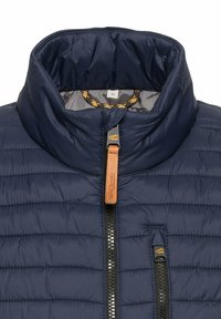 Granatowa kurtka typu puchowa z wysokim kołnierzem, zamkiem z przodu i skórzanym uchwytem suwaka. Posiada pikowany wzór oraz dodatkową kieszeń zapinaną na zamek.