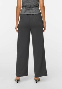 Szare szerokie spodnie o gładkiej fakturze i elastycznym pasku w talii, w zestawieniu z dopasowaną szarością górą. Na dole widoczne szpilki.