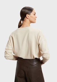 Beige pletený svetr s volným střihem, kulatým výstřihem a žebrovanými manžetami, doplněný tmavě hnědými koženými kalhotami s vysokým pasem.