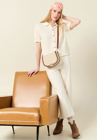 Krämfärgad stickad skjorta med korta ärmar och knappar, i kombination med högmidjade vita byxor. Bruna ankelstövlar och en blommig huvudscarf.