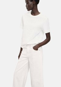 White cotton t-shirt with a round neckline, short sleeves, paired with white wide-leg jeans featuring front pockets and metal accents.