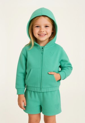 Sweat à capuche zippé vert clair avec une poche kangourou, associé à un short assorti, présentant un détail de broderie en forme de cœur, fabriqué en tissu doux.