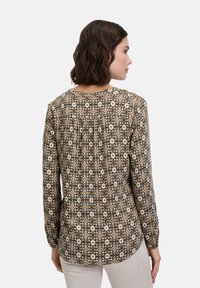 Langarmbluse in Schwarz, Beige und Creme mit floralem Muster. Verfügt über einen runden Ausschnitt und einen gefalteten Rückendetail. Glatte Stofftextur.
