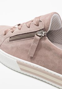 Jasnoróżowe zamszowe sneakersy z sznurowanymi detalami, boku z zamkiem błyskawicznym oraz białą gumową podeszwą z delikatnymi paskami. Teksturowana cholewka.