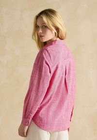 Ružová kockovaná košeľa na gombíky vyrobená z ľahkej látky, s dlhými rukávmi, golierom a detailom v zadnej časti v podobe plisovania.