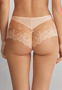 Perzikkleurige kant lingerie met een doorzichtige mesh achterkant, voorzien van bloemenpatronen langs de randen en gegolfde zoom. Zachte, delicate textuur.