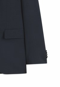 Manche et côté de veste de costume bleu marine foncé avec poche à rabat et quatre boutons de manchette sur fond blanc.