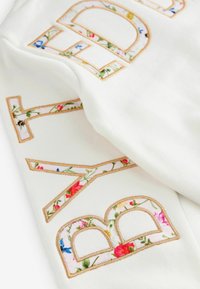 Weißer Sweatshirt mit auffälligen, gestickten Buchstaben und floralen Mustern, versehen mit goldenen Nähten, der eine glatte Textur und eine lockere Passform bietet.