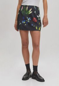 Mini-rok met een bloemenprint op een zwarte achtergrond; heeft kleurrijke tulpen, madeliefjes en groen; gemaakt van een gladde stof.