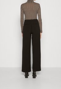 Svarta vidbyxor med en slät textur, som har två bakfickor. Tillsammans med en långärmad topp i svart och beige med ränder.