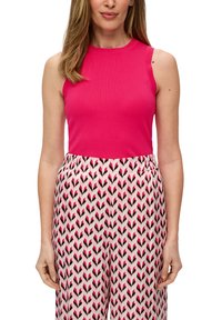 Fuchsia mouwloze top gecombineerd met patroon brede broek met roze en zwarte zigzagontwerpen op een witte achtergrond.