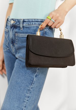 Zwarte clutch handtas met een soepele textuur, voorzien van een klep sluiting en een gouden kettinghandvat. Draagt met blauwe hoogwaist jeans.