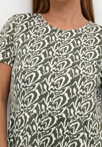 Zielona bawełniana koszula z białym abstrakcyjnym wzorem, okrągłym dekoltem, krótkimi rękawami i lekko luźnym krojem.