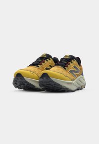 Trail løbesko med en gul og sort mesh-overdel, tyk grå sål, teksturerede detaljer og sort gummisål med traction-lugger.