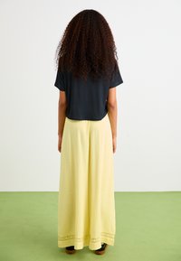 Zwarte top met korte mouwen gecombineerd met een lange gele gestructureerde rok met kantafwerking aan de onderkant. Draag met donkere schoenen.