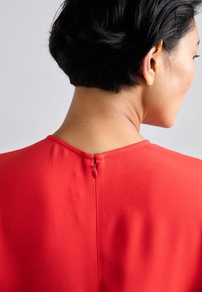 Vestido rojo con cuello alto y cremallera oculta en la espalda. Textura de tela suave y diseño minimalista, con líneas limpias.