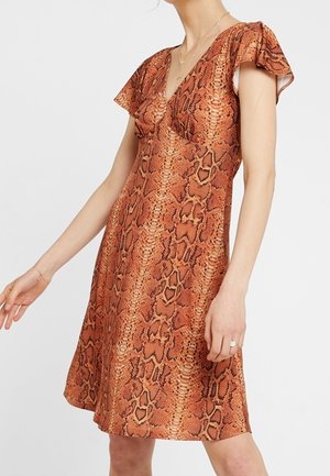 Femme portant une robe à manches courtes et col en V avec un imprimé serpent marron et orange.