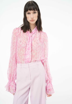 Blusa rosa trasparente con collo a cravatta e maniche a campana; presenta una delicata stampa animale. Abbinata a pantaloni alta vita rosa chiaro.