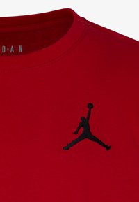 Červené bavlněné tričko s černým vyšívaným logem Jumpman na levé části hrudi. Kulatý výstřih s jemným žebrováním.