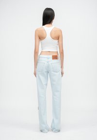 Jeans de mezclilla azul claro con un corte holgado, que cuentan con dos bolsillos traseros y una etiqueta de cuero marrón en la cinturilla. Top corto blanco visible.