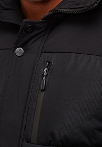 Černá prošívaná bunda s uzávěrem na zip, patentkou a texturovanou tkaninou s elegantním povrchem. Obsahuje kapsu na zip.